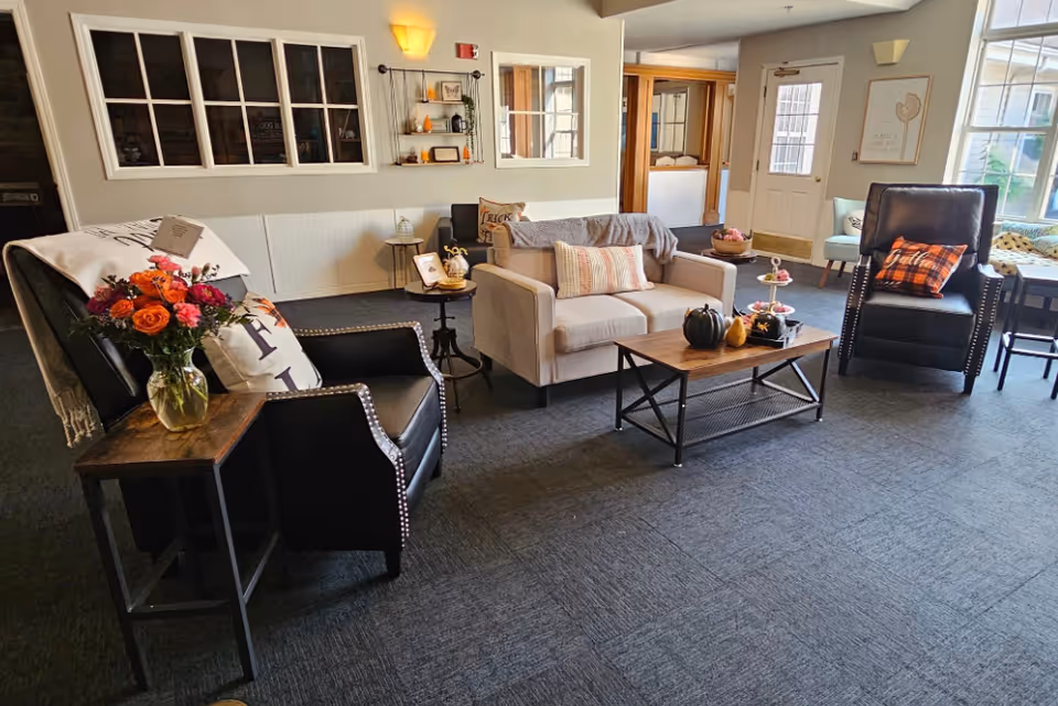 Cozy lounge with sofas, chairs, coffee table, fall decor in a senior living facility.
