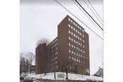 Tall brick high-rise building in a snowy urban setting, viewed from the street.