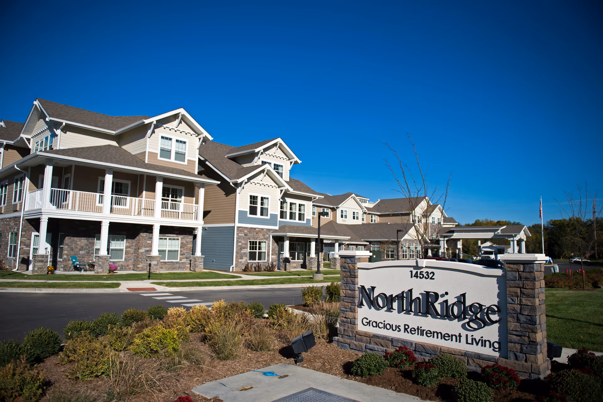 Exterior view of a multi-story senior living building with a stone sign reading "NorthRidge Gracious Retirement Living" in the foreground under a clear blue sky.