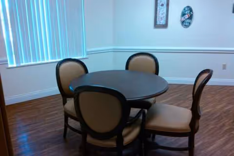 Round dining table with four chairs in a well-lit senior living dining area.