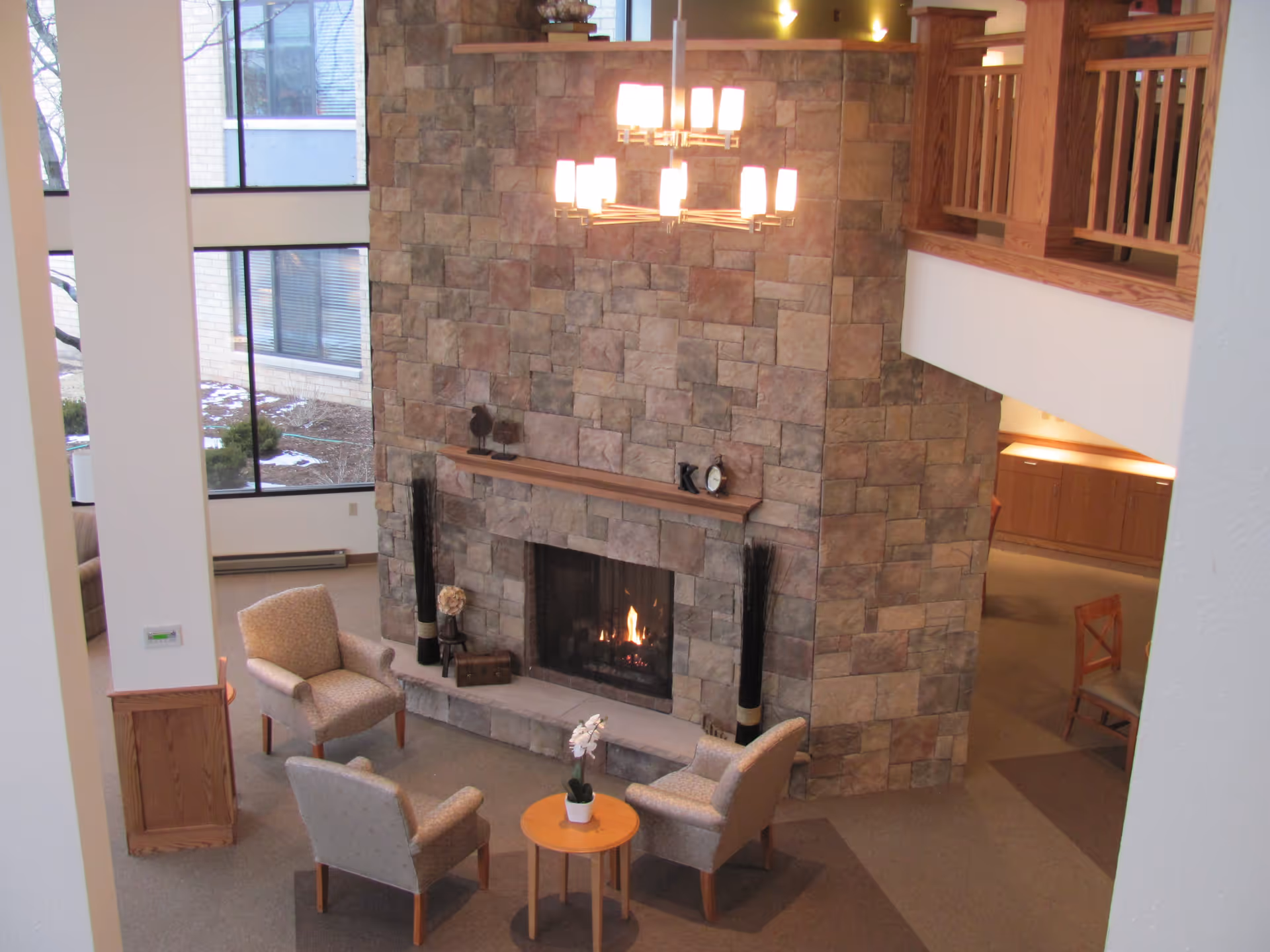 Interior lounge with a large stone fireplace, four upholstered chairs arranged around a small round table and a hanging chandelier.