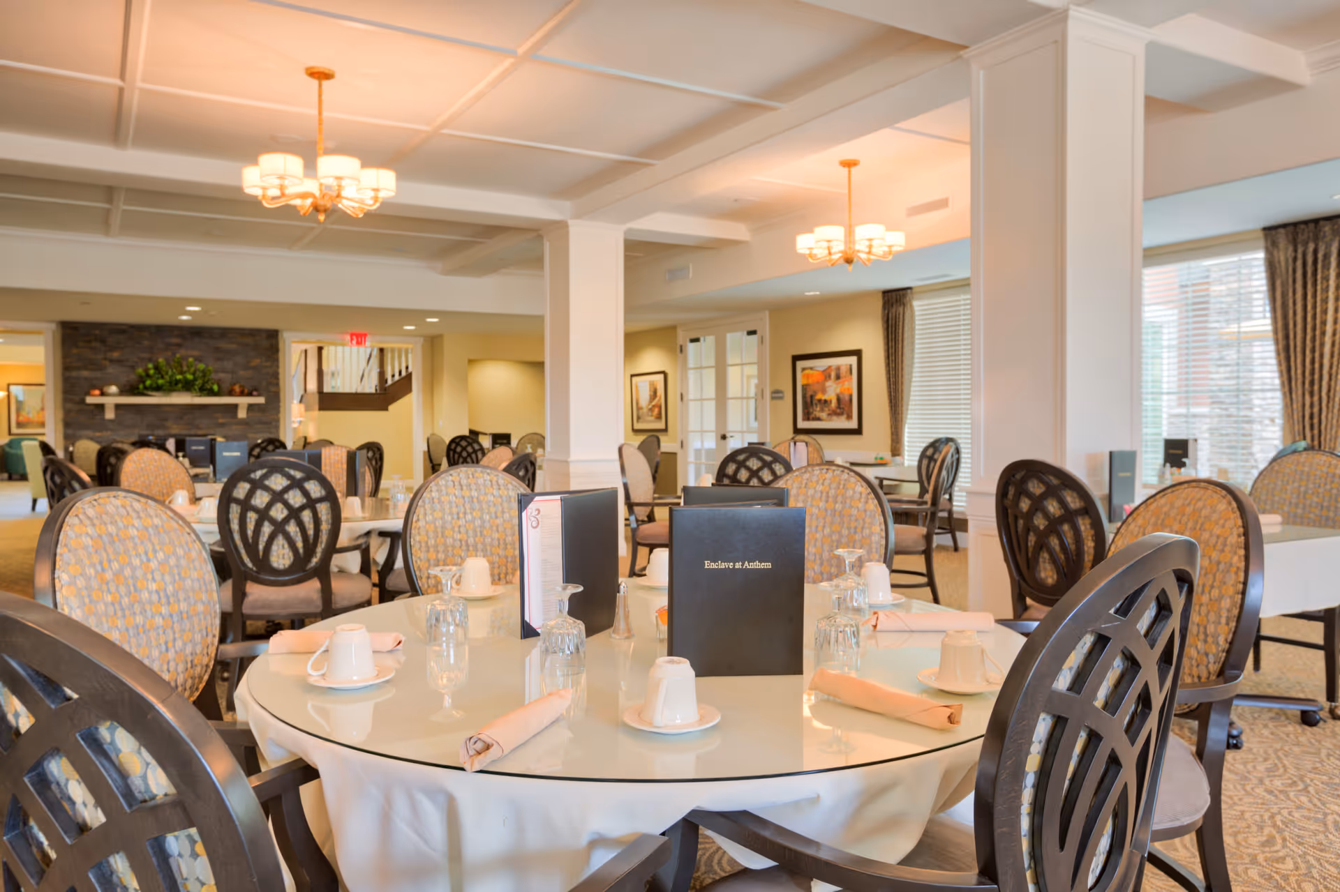 Bright, formal dining room with round tables set with place settings and menus reading 'Enclave at Anthem'.
