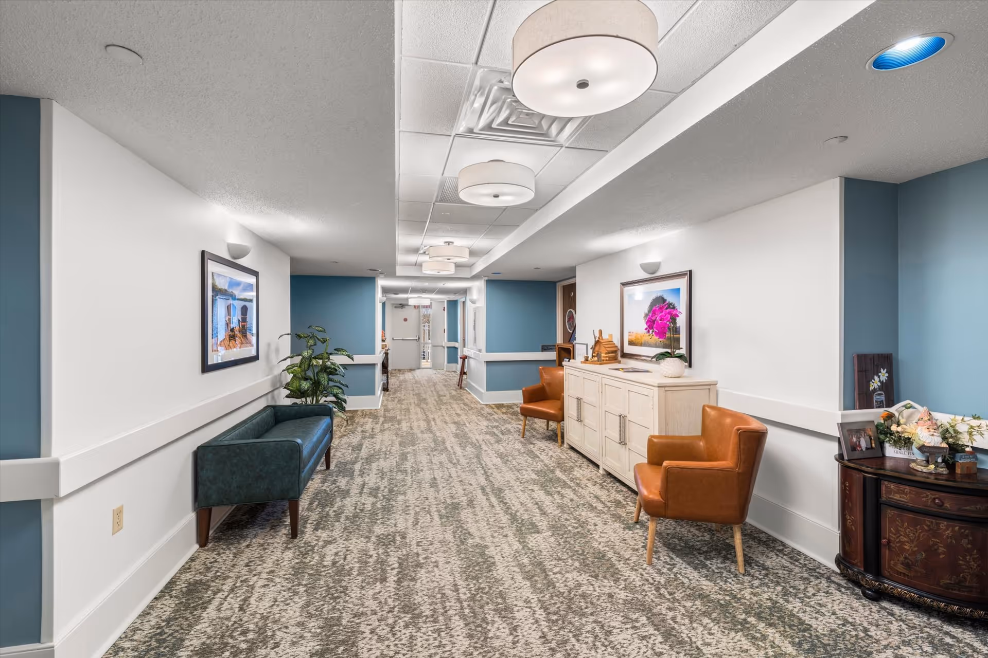 Well-lit interior hallway with seating, artwork, cabinets, and decorative accents.