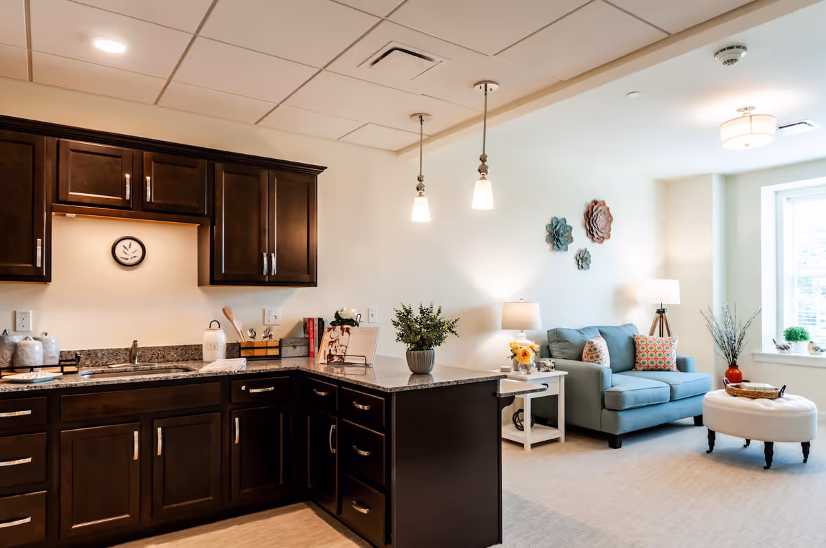 Open-concept kitchen and living area with dark wood cabinets, a granite countertop island, and a light-blue sofa by a window.