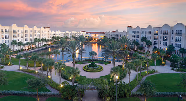 Landscaped courtyard with a central pond and palm trees surrounded by multi-story residential buildings at sunset.