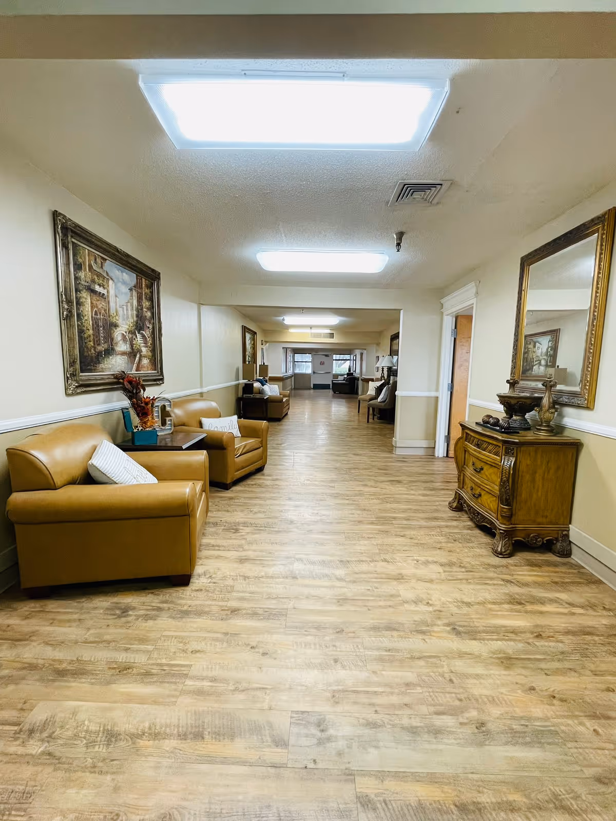 Long interior hallway/common lounge with leather chairs, artwork, and wood-look flooring.