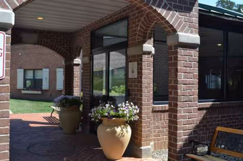 Brick building entrance with large glass doors, potted flowers, and a bench.