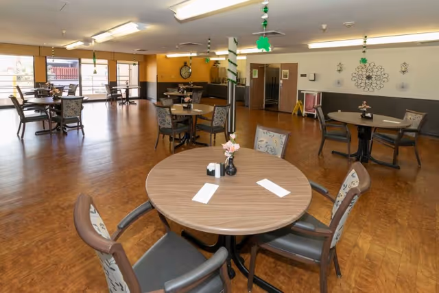 Spacious senior dining room with round tables and chairs, wood flooring, and hanging shamrock decorations.