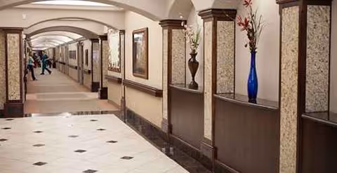 Long interior corridor with arches, columns, framed art, and decorative vases along walls.