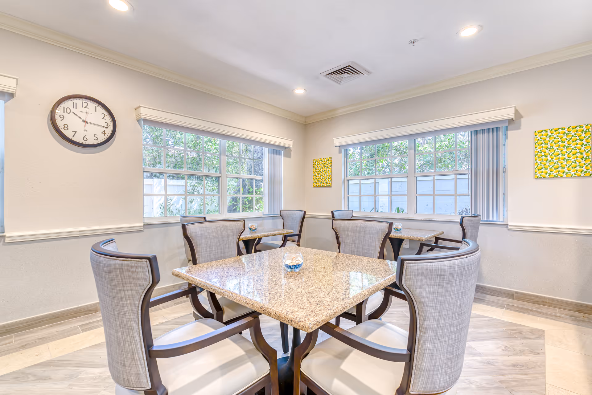 Bright communal dining room with granite-top tables and upholstered chairs by large windows.