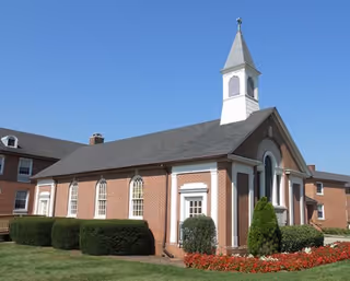 Front view of a brick senior living facility with a white steeple and manicured landscaping.