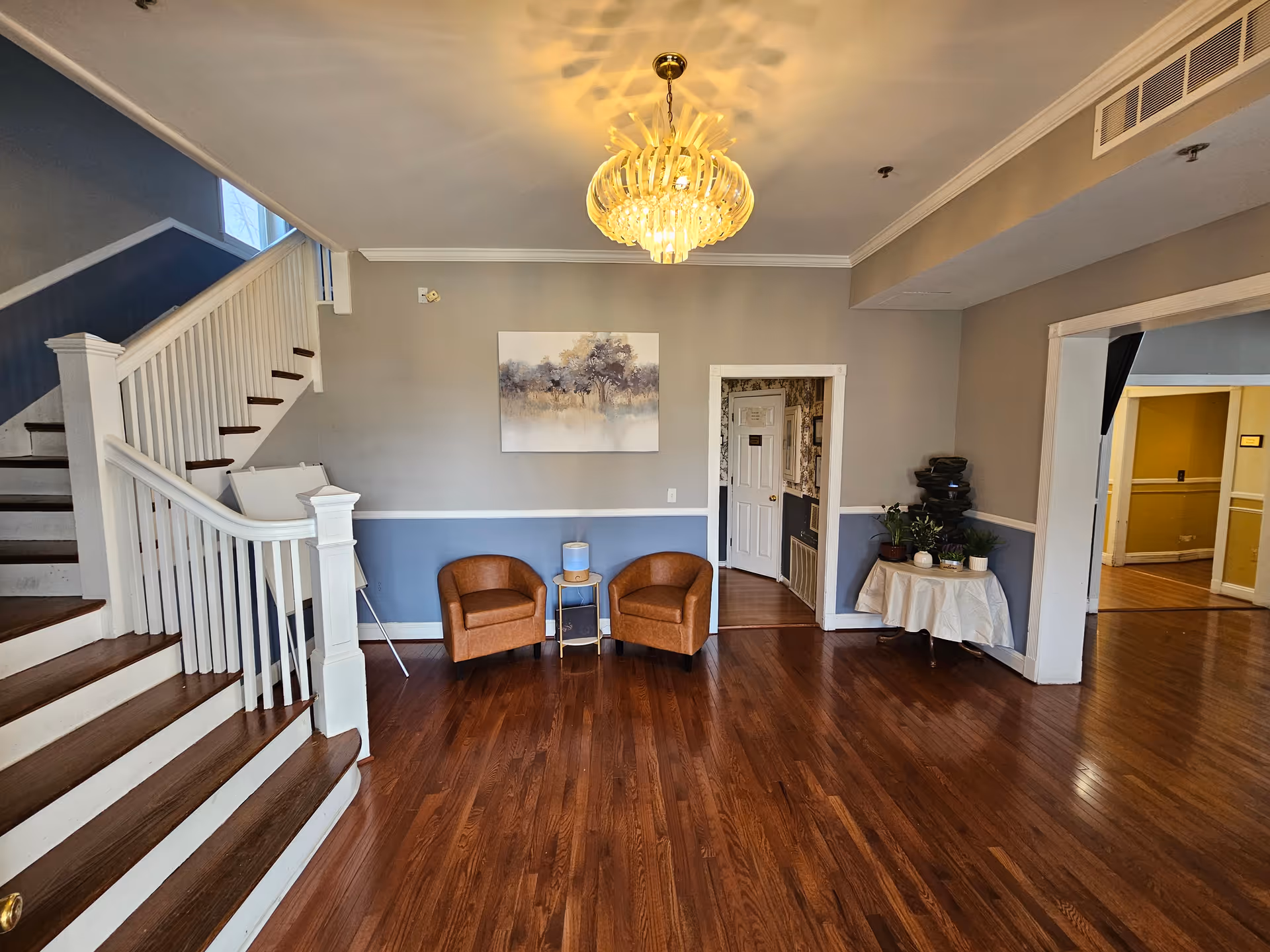 Lobby of Rolling Meadows Assisted Living with staircase, chandelier, two chairs, and a table.