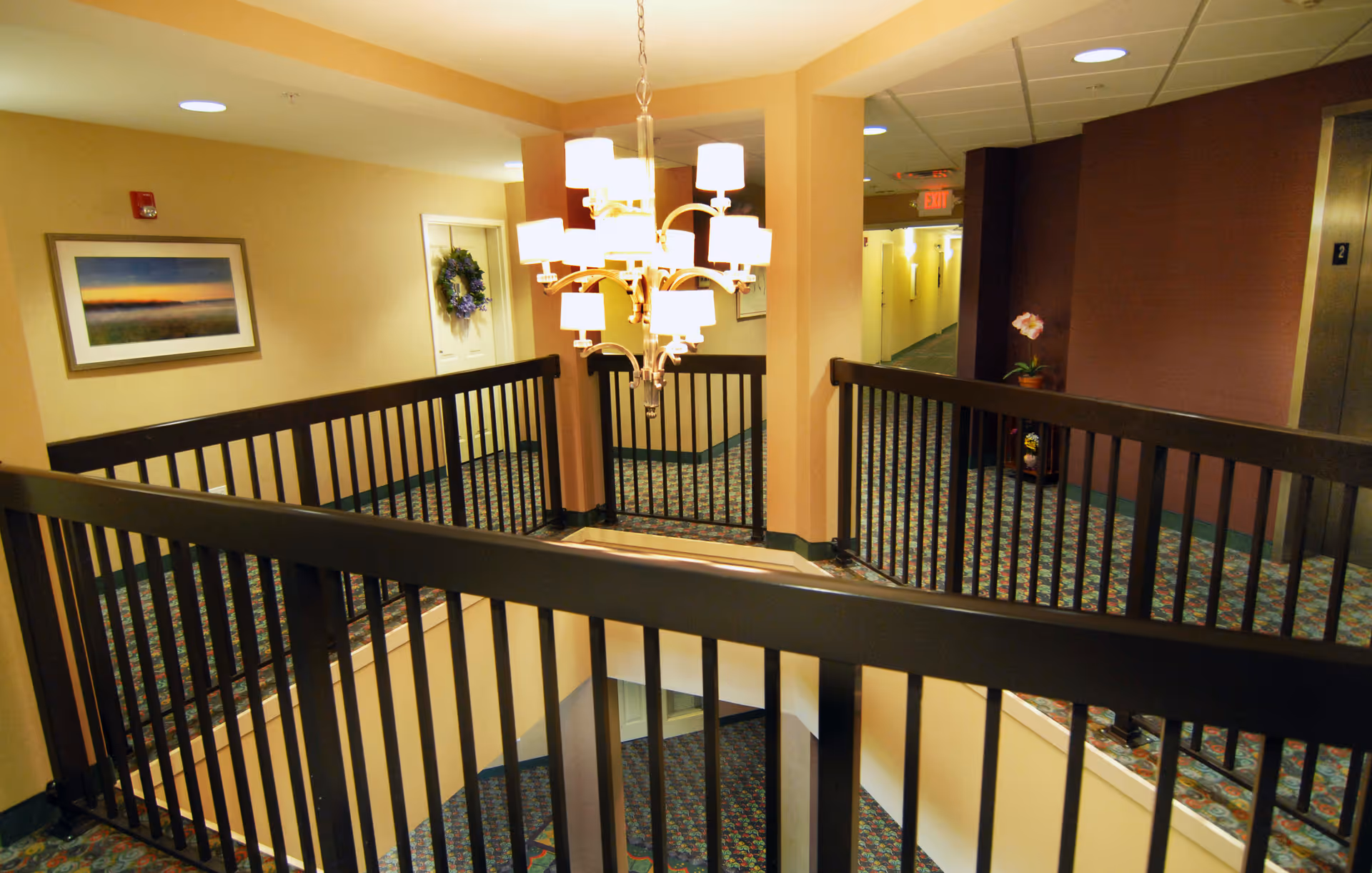 Carpeted interior hallway and second-floor landing with dark railings, a central chandelier, and doors leading to rooms.