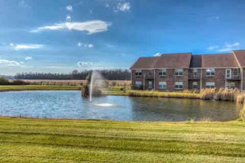 Reflections Retirement Community exterior with brick building, pond, fountain, and manicured lawn.