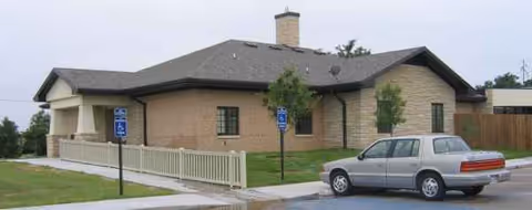Exterior view of a single-story brick senior care facility with a parked car.