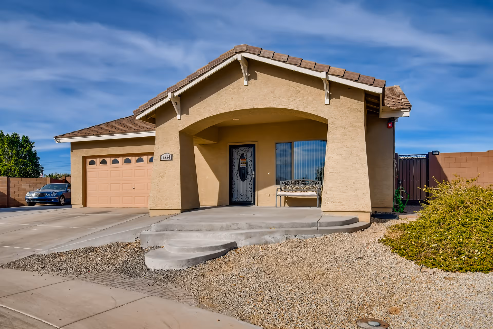 Front exterior of a single-story beige stucco house with a covered porch, attached garage and driveway.