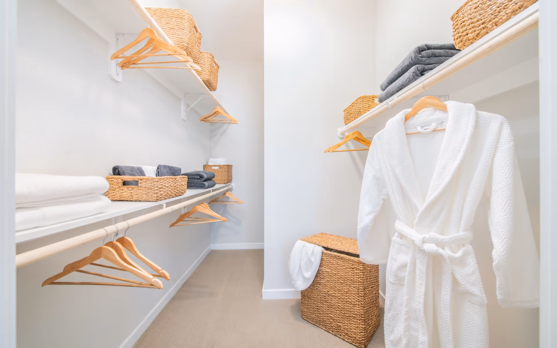 Well-organized walk-in closet with shelves, wooden hangers, woven baskets, folded towels, and a white bathrobe hanging.