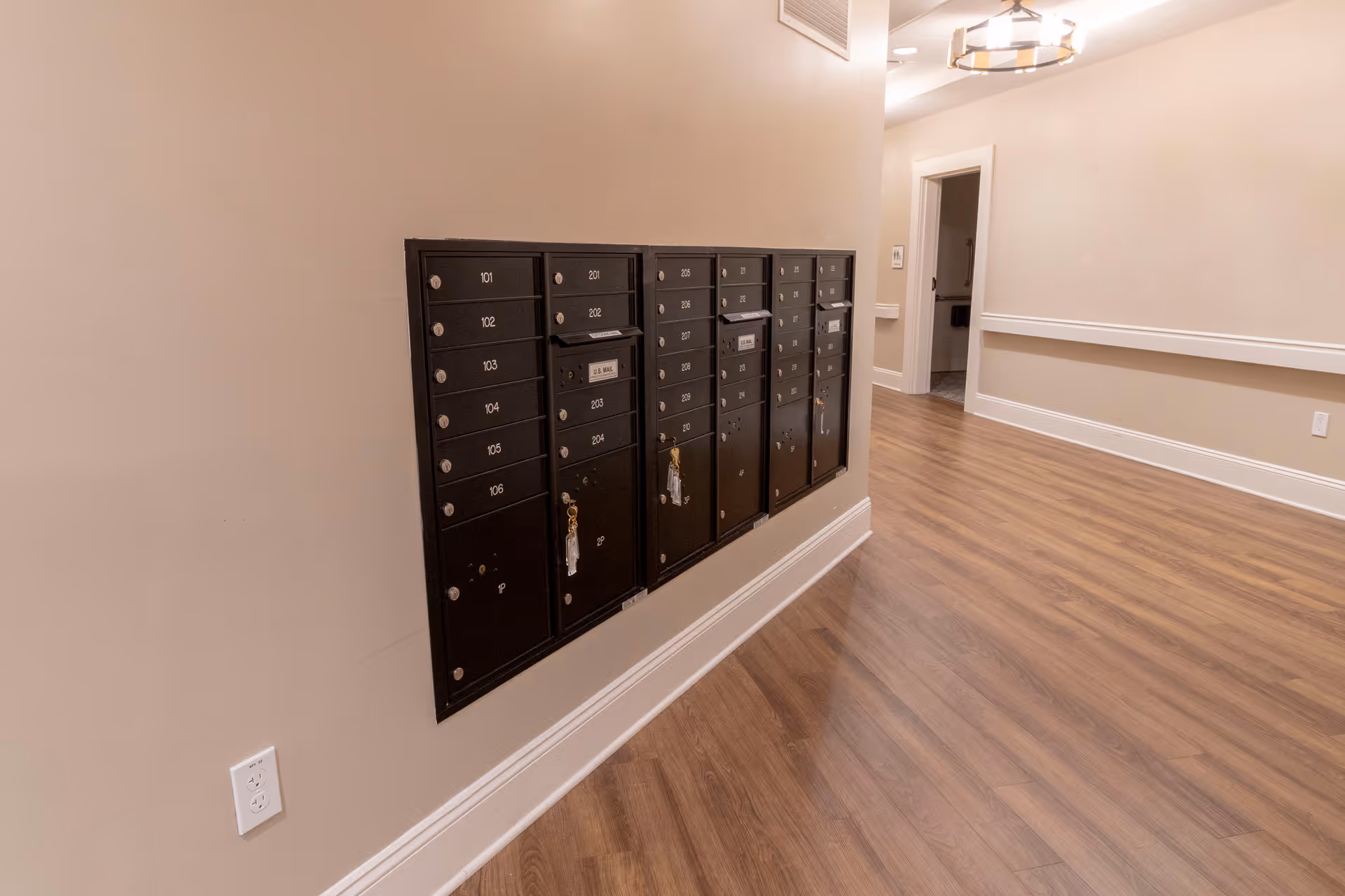 Wall-mounted resident mailboxes along a hallway with wood flooring and beige walls.