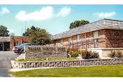 Front view of a single-story brick senior living facility with a terraced lawn, stone retaining wall, and parked cars.