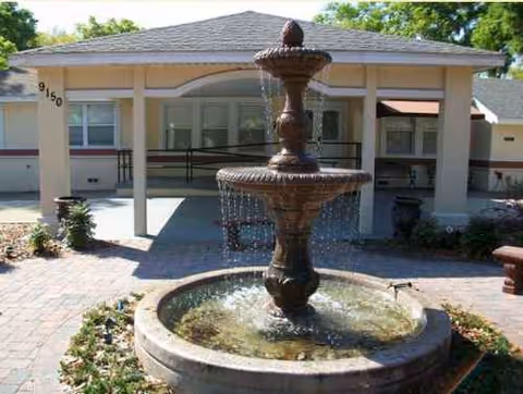 Stone fountain in a brick courtyard in front of a single-story assisted living building.