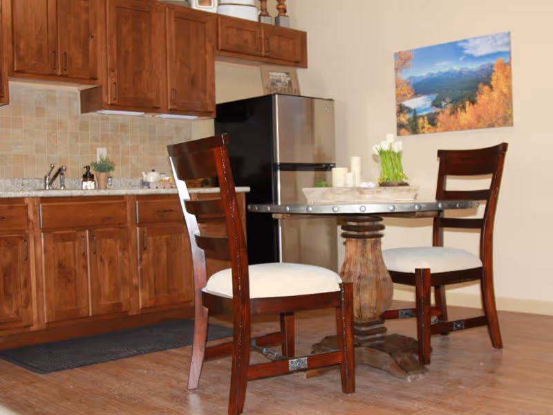Small kitchen area with wooden cabinets, a stainless steel refrigerator, and a round dining table with two chairs.