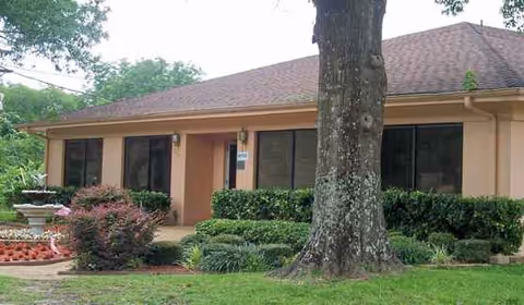Single-story beige senior living facility exterior with large windows and landscaping.