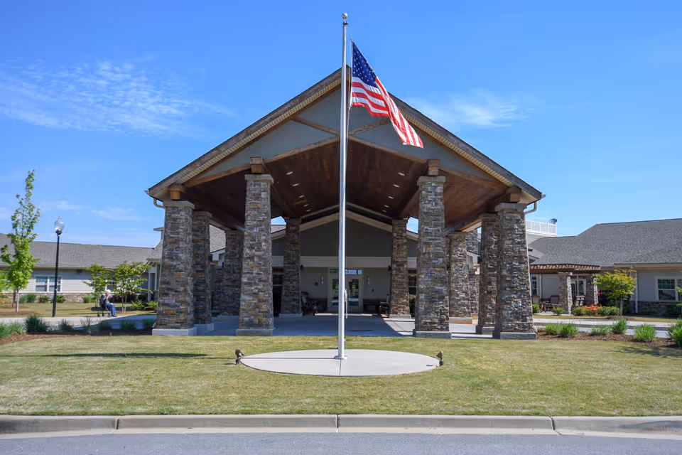 The entrance of Oakview Park featuring a large covered area supported by stone pillars, with an American flag flying in front and landscaped greenery surrounding the entrance.