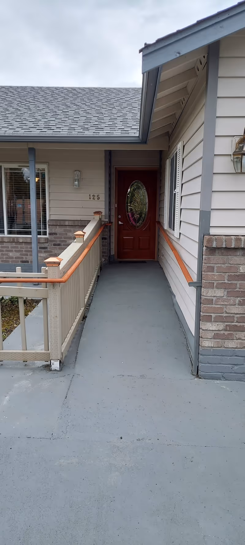 Front entrance walkway with a ramp leading to a red oval-glass door on a single-story house numbered 125.