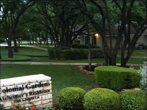 Outdoor landscaped courtyard with bushes, trees, and a stone sign in front of a building.