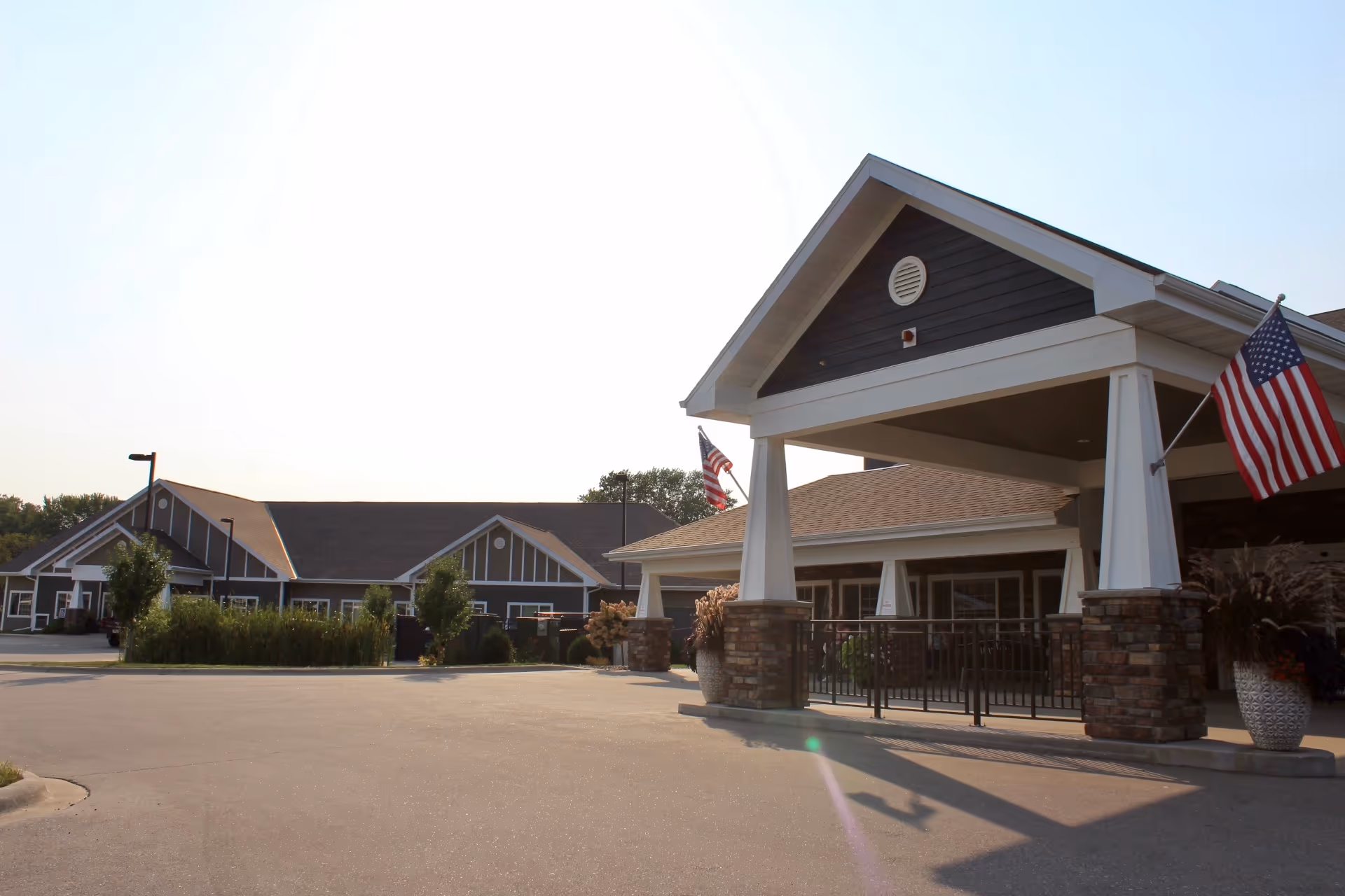 Front view of a senior living facility with a covered entrance and American flags.