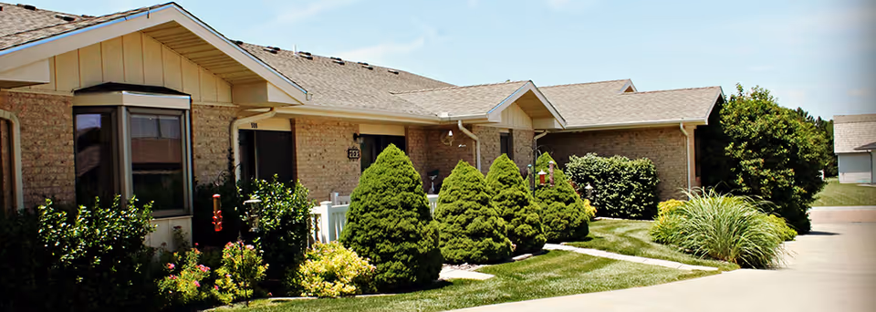 Exterior view of a single-story brick building with a row of neatly trimmed bushes and green lawn in front, under a clear blue sky.