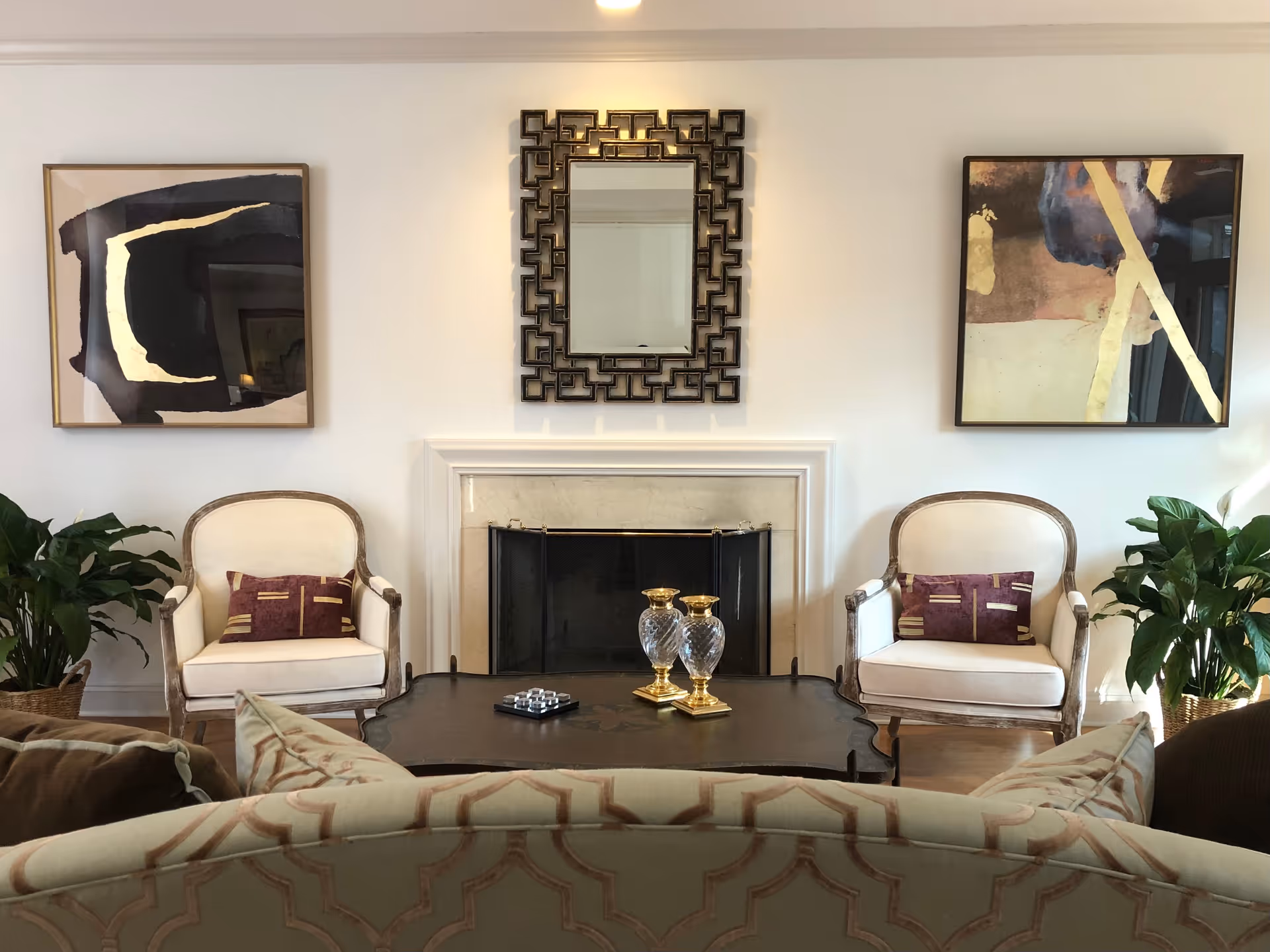 Stylish living room with a fireplace flanked by two armchairs, a decorative mirror and artwork above, and a coffee table in front.