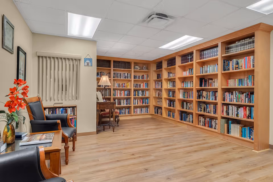 Cozy reading room with wall-to-wall wooden bookshelves, hardwood floor, and leather chairs with a small table and lamp.