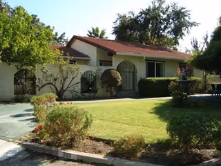 Front view of Belrose Care Home, a single-story building with manicured lawn and shrubs.
