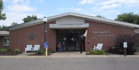 Brick building with glass doors, Birchwood Apartments sign, benches and accessibility sign outside.