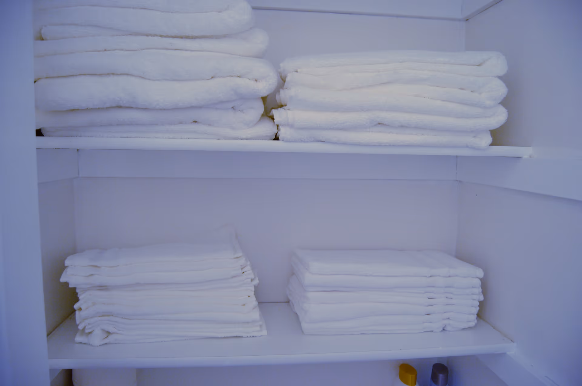 White folded towels neatly stacked on white shelves inside a linen closet or storage area.