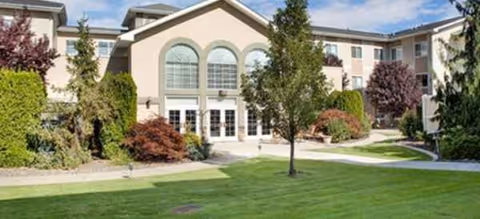 Exterior view of Rexford Park senior living building with a green lawn and trees.
