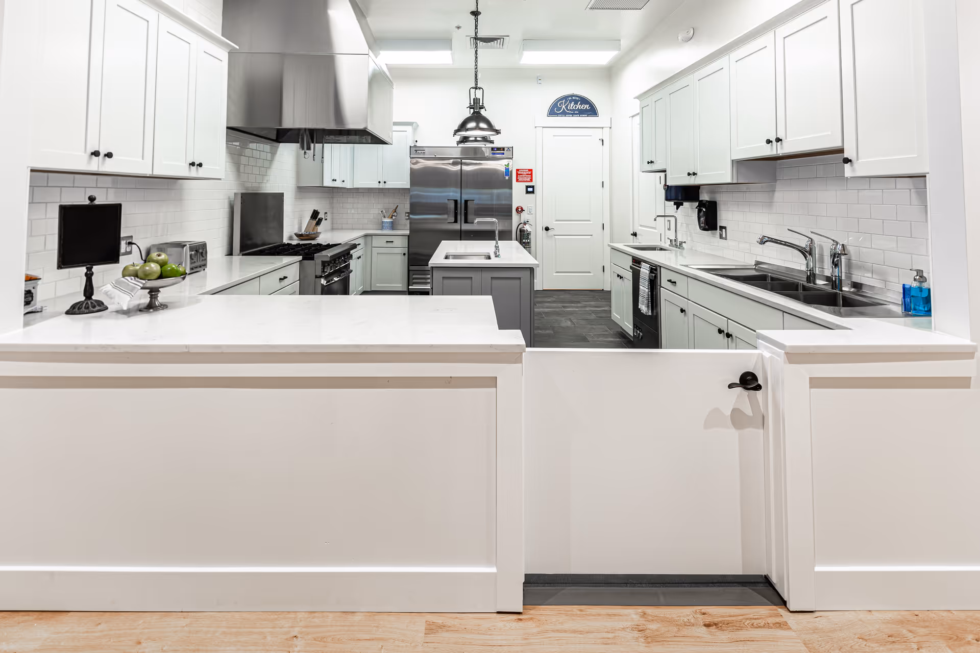 Bright, modern communal kitchen with white cabinets, stainless steel appliances, a center island and a pass-through counter with a half-door.