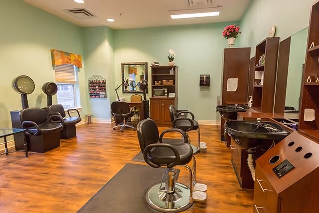 Interior salon with styling chairs, shampoo sinks, hooded dryers and cabinetry on a wood floor.