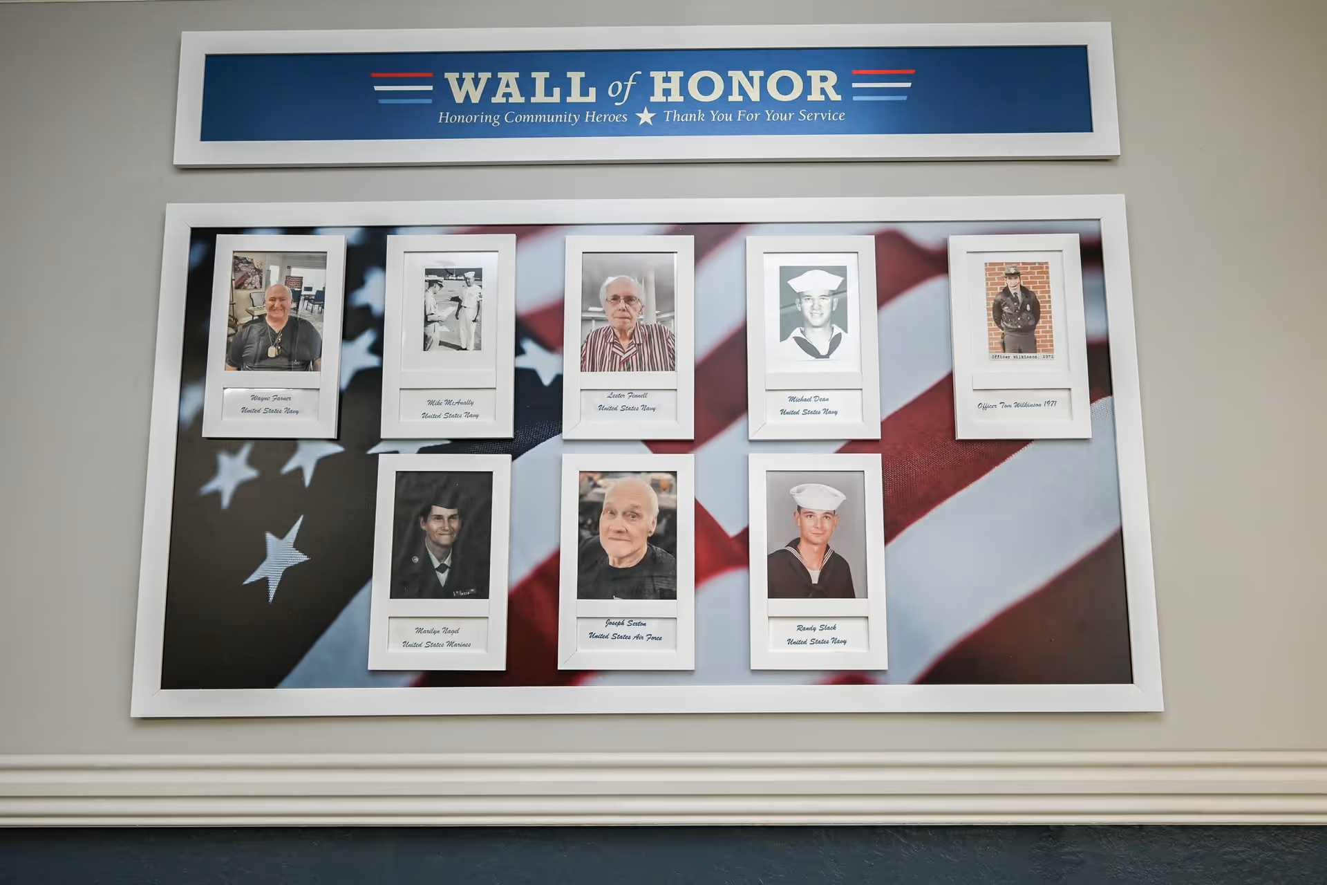 Framed portraits of veterans displayed on a 'Wall of Honor' plaque with an American flag backdrop mounted on an interior wall.
