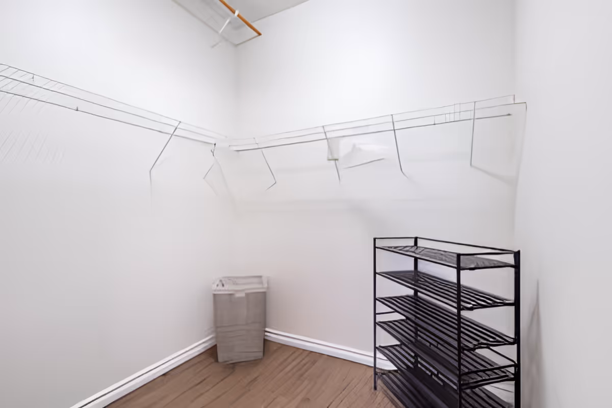 Empty walk-in closet with white wire shelving, a laundry hamper, and a black metal shoe rack.