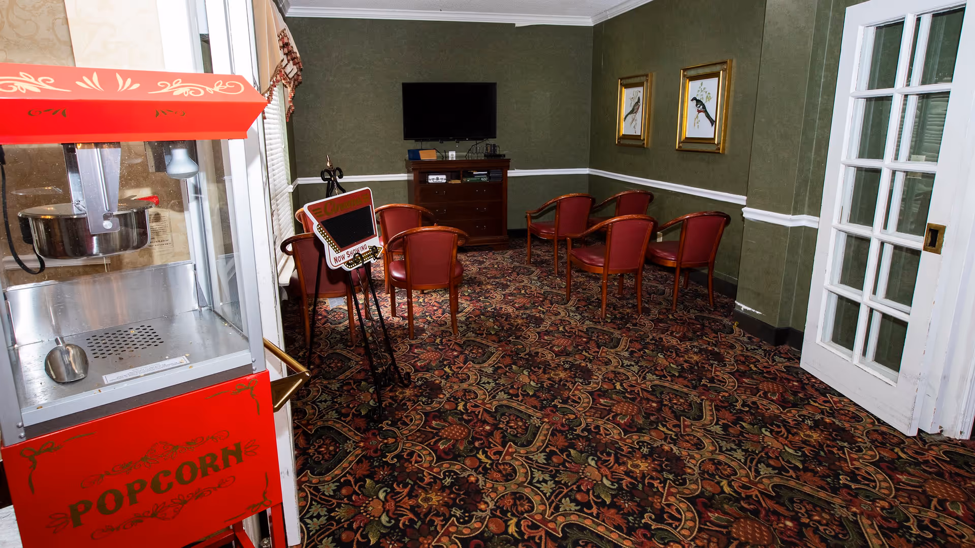 Carpeted common room with red chairs arranged facing a wall-mounted TV and a popcorn machine in the foreground.