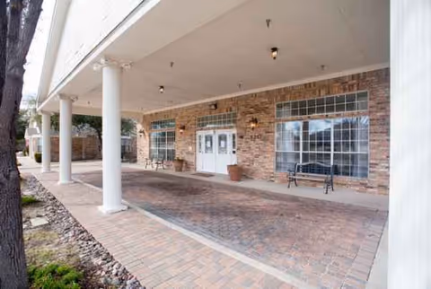 Covered brick-front entrance with white columns, benches, and glass doors.