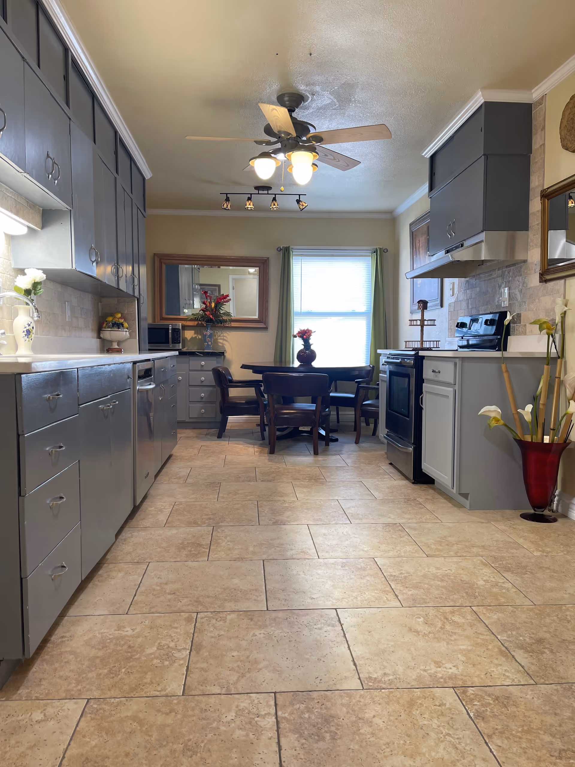 Bright kitchen with gray cabinets, tiled floor, stove, and a small dining table by a window.