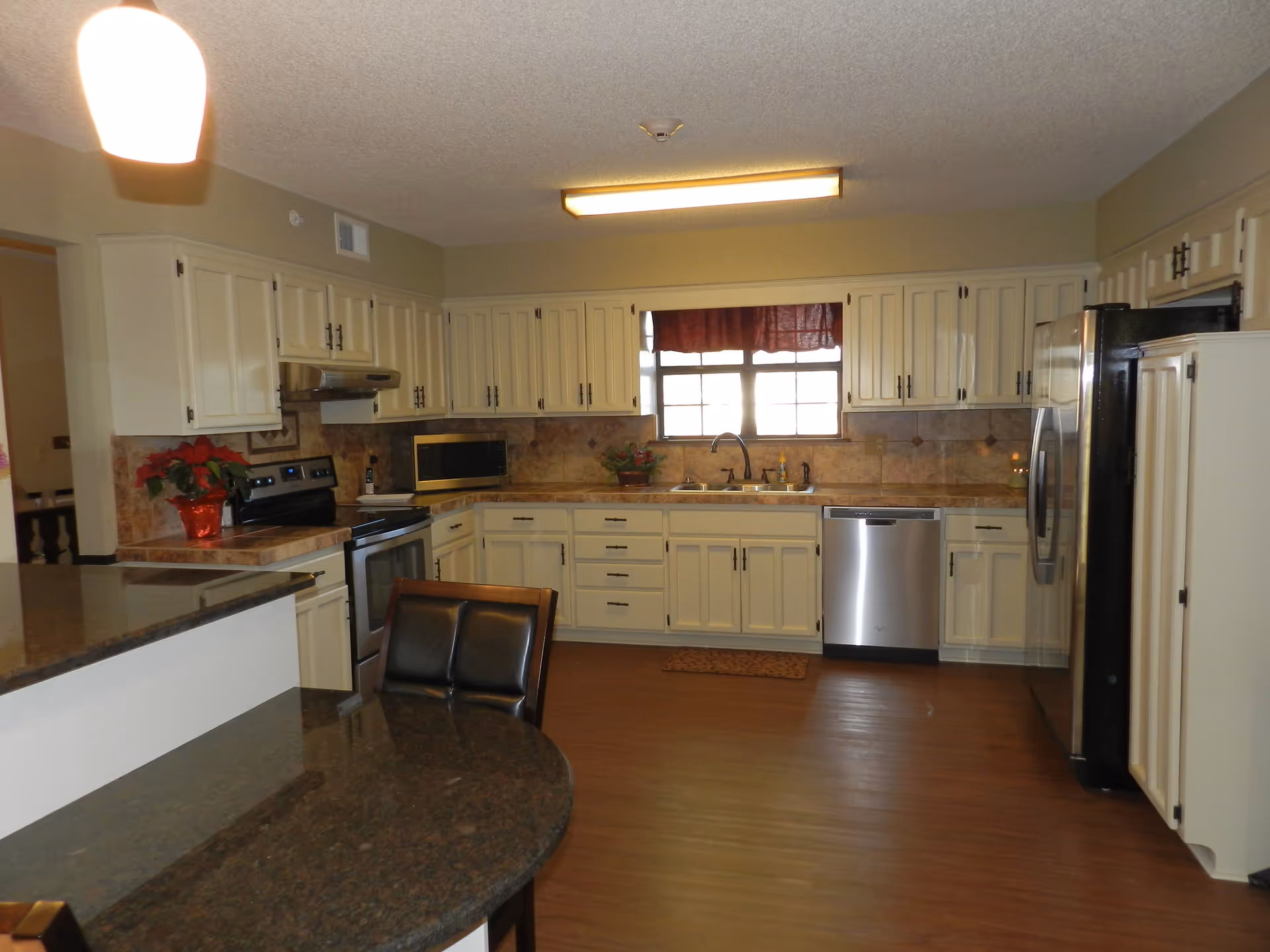 Well-lit kitchen with white cabinets, stainless steel appliances, dark granite countertops and a small island with seating.