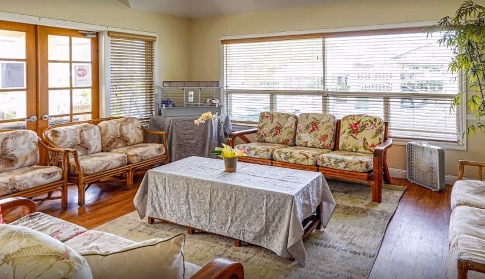 Bright lounge area with floral couches around a coffee table and large windows.