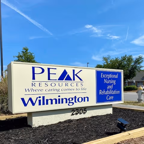 Outdoor sign reading 'PEAK Resources Wilmington' and 'Exceptional Nursing and Rehabilitation Care' in front of the facility under a blue sky.
