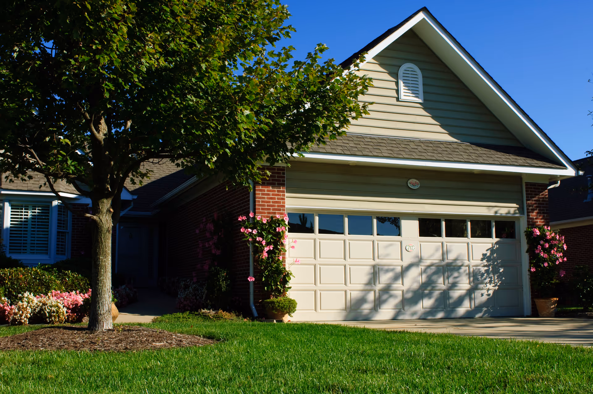 Front view of a facility-style building with a large garage, tree, and manicured lawn.