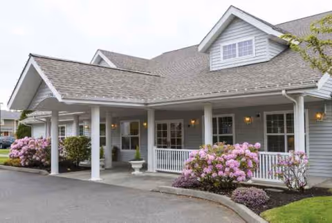 Front exterior of Avista Senior Living Ferndale with a covered entrance and pink shrubs.