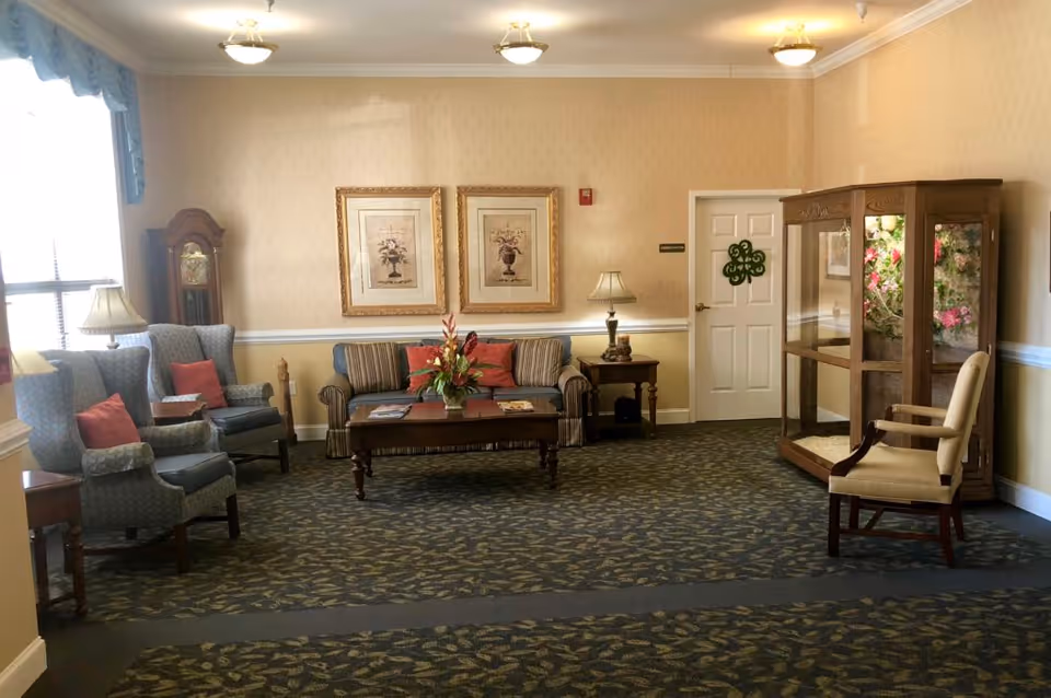 Cozy sitting room with armchairs, a striped sofa, coffee table, lamps, a grandfather clock and a glass display cabinet.